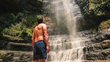 Man looking up at waterfall in jungle.
